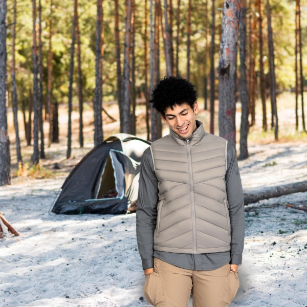 Man wearing a beige lightweight down vest in a forest campsite, showcasing WHFrontend’s outdoor clothing design for layering comfort and warmth.